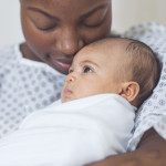 Beautiful African American mother in a hospital gown holds her newborn baby