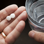 Hands holding two aspirin and a glass of water