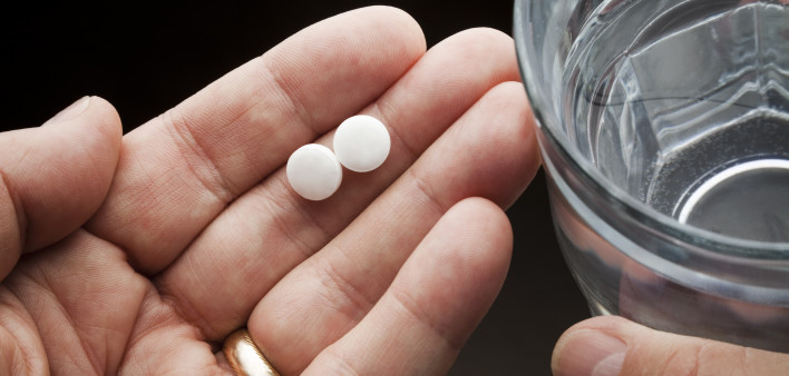 Hands holding two aspirin and a glass of water