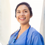 Young adult Hispanic woman is smiling while standing outside on college campus.