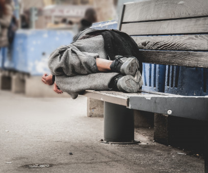 Poor homeless man or refugee sleeping on the wooden bench on the urban street in the city,