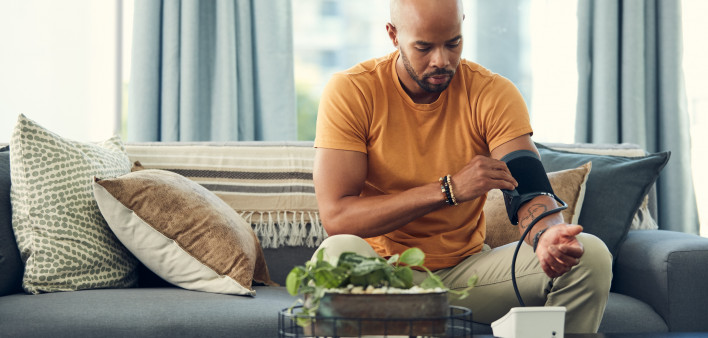 Shot of a young man taking his blood pressure while sitting on the sofa at home