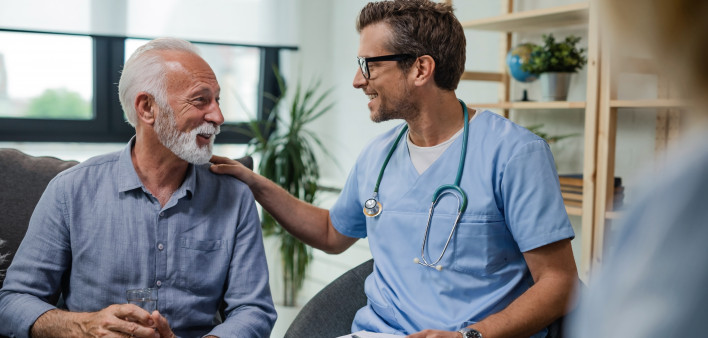 Happy doctor talking to senior male patient while being in a home visit.