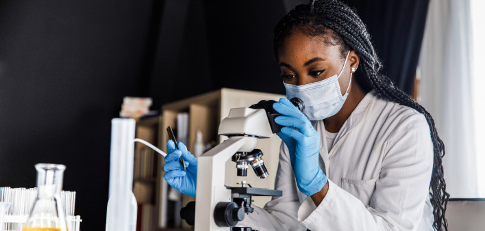 female scienitst analyzing a sample under a microscope while doing research