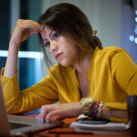 Young woman with laptop computer for homework. Tired hispanic girl and college education. Female student studying and using pc at home getting headache