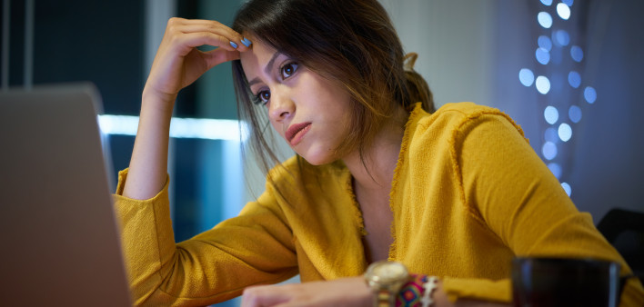 Young woman with laptop computer for homework. Tired hispanic girl and college education. Female student studying and using pc at home getting headache
