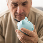 Senior caucasian man holding piggy bank with glasses depressed and worry for distress, crying angry and afraid.