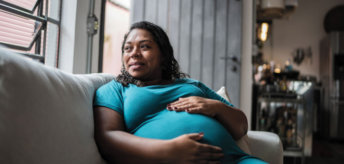 Pregnant Black woman holder her belly on couch