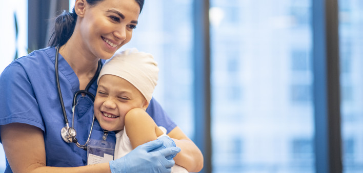 Nurse Hugging Young Cancer Patient stock photo A young Latin female nurse hugs her cancer patient as they enjoy a brief moment together. The young girl is smiling and happy. The nurse is wearing blue scrubs with a stethoscope around her neck, while the yo