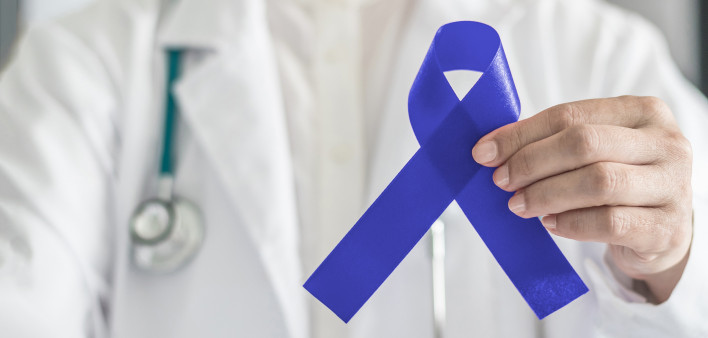 Dark blue ribbon for colon - colorectal cancer awareness on medical doctor's hand