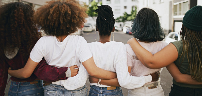 Rearview shot of a group of unrecognizable young friends walking with their arms around each other in the city