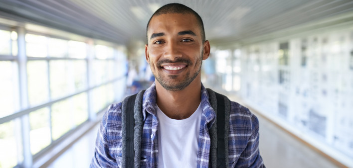 Portrait of a happy young man standing in a corridor on campus