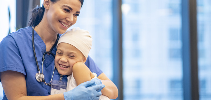 Nurse Hugging Young Cancer Patient stock photo A young Latin female nurse hugs her cancer patient as they enjoy a brief moment together. The young girl is smiling and happy. The nurse is wearing blue scrubs with a stethoscope around her neck, while the yo