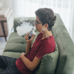 Young man vaping e-cigarette at home