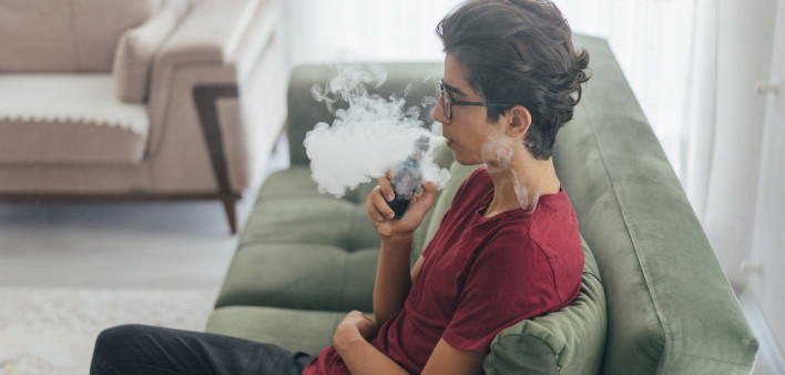 Young man vaping e-cigarette at home