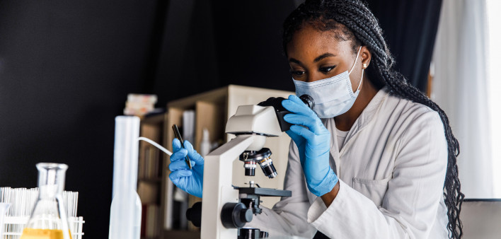 female scienitst analyzing a sample under a microscope while doing research