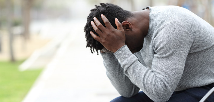 Side view portrait of a sad depressed black man sitting on a bench in a park