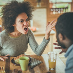 Angry African American woman arguing with her husband at dining table.