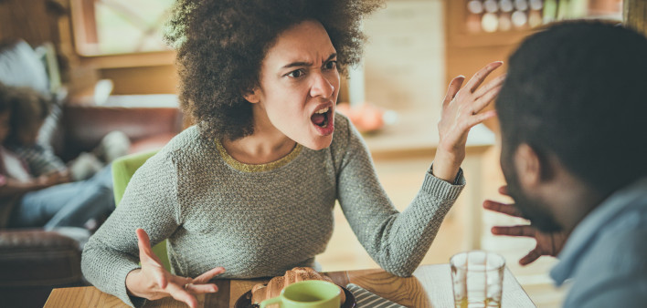 Angry African American woman arguing with her husband at dining table.