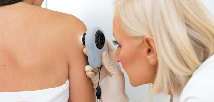 Female dermatologist examining female patient's skin with dermascope, doctor is carefully looking for signs of skin cancer