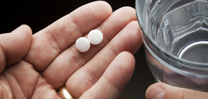 Hands holding two aspirin and a glass of water