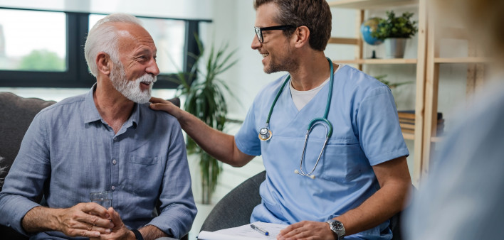 Happy doctor talking to senior male patient while being in a home visit.