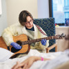 music therapy woman playing guitar to person in hospital bed