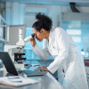 woman scientist in white lab coat looking into a microscope