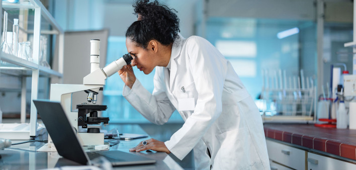 woman scientist in white lab coat looking into a microscope