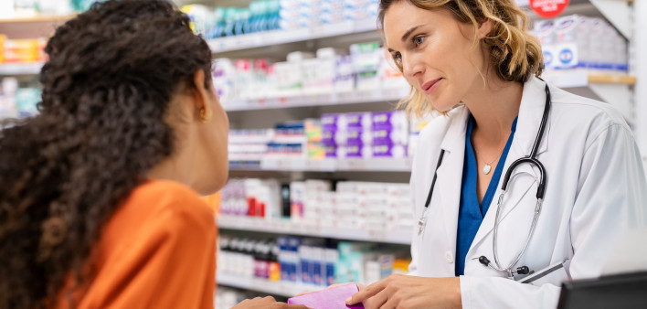 Pharmacist giving medicine box to customer in pharmacy. Doctor showing and explaining medicine dose to customer. Mature pharmacist giving advice on medicaments, while serving young african woman.
