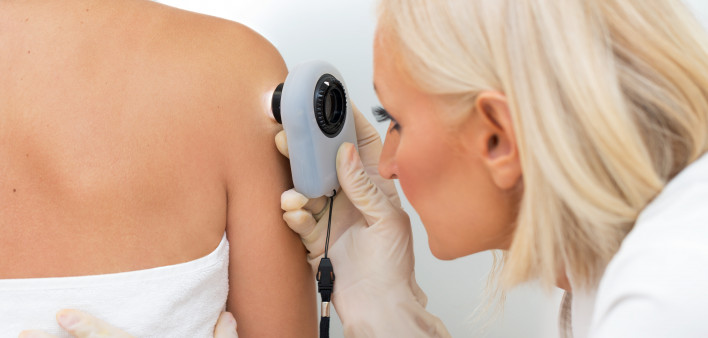 Female dermatologist examining female patient's skin with dermascope, doctor is carefully looking for signs of skin cancer