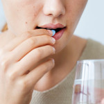 Girl taking a blue pill with glass water