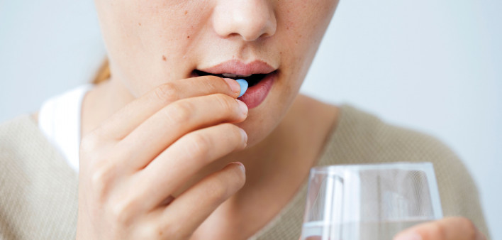 Girl taking a blue pill with glass water