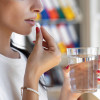 Woman taking a white pill with a glass of water