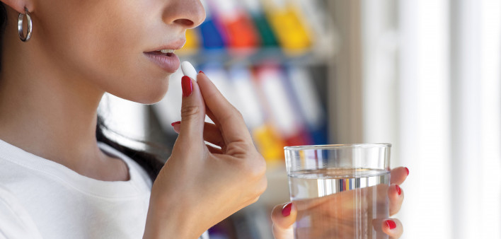 Woman taking a white pill with a glass of water