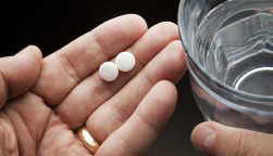 Hands holding two aspirin and a glass of water