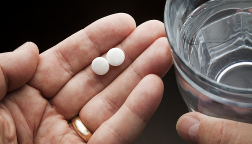 Hands holding two aspirin and a glass of water
