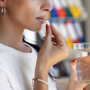 Woman taking a white pill with a glass of water