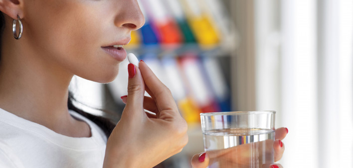 Woman taking a white pill with a glass of water
