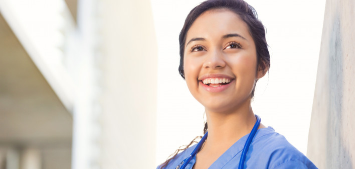 Young adult Hispanic woman is smiling while standing outside on college campus.