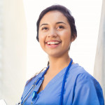 Young adult Hispanic woman is smiling while standing outside on college campus.