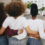 Rearview shot of a group of unrecognizable young friends walking with their arms around each other in the city