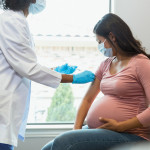 Expectant mother watches as tech gives her vaccine
