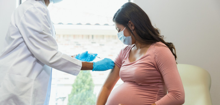 Expectant mother watches as tech gives her vaccine