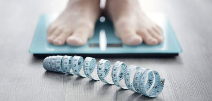 mans feet on scale with measuring tape on floor