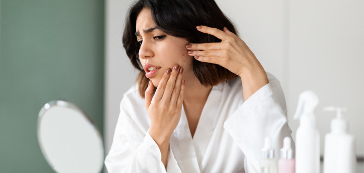 looking at mirror, checking skin, touching her cheek, home interior. Acne, pimples, dull skin