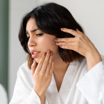 looking at mirror, checking skin, touching her cheek, home interior. Acne, pimples, dull skin