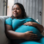 Pregnant Black woman holder her belly on couch