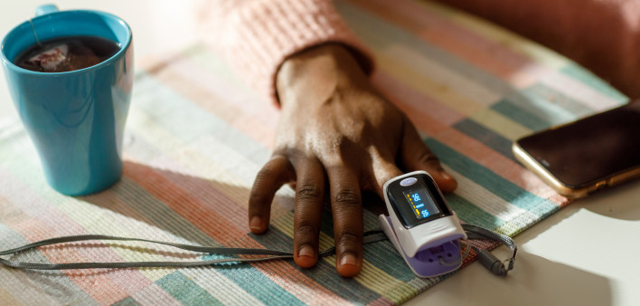 A black black woman measures her oxygen level at home using a pulse oximeter.