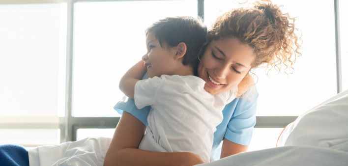 Beautiful sweet little boy hospitalized in the pediatrics ward hugging young nurse both smiling
